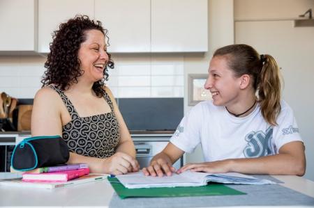Young person and parent sit together at kitchen table with exercise book and pencil case.