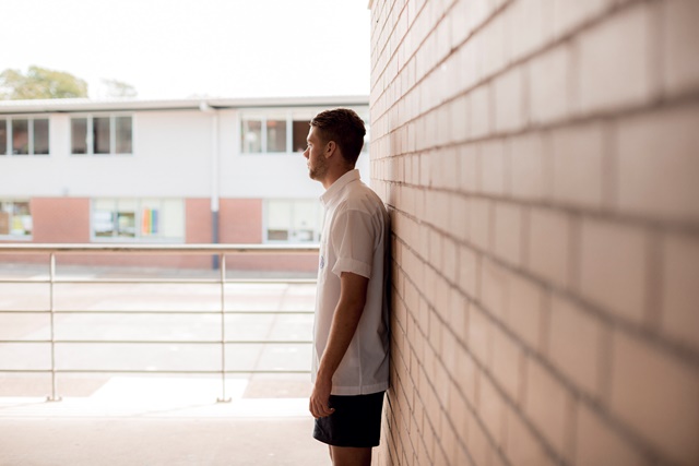 Side profile of young person leaning against brick wall